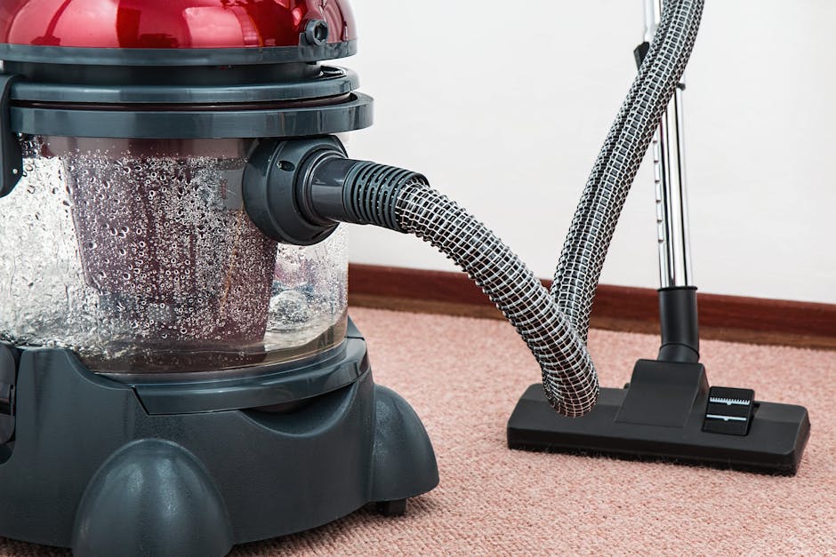 A woman using a yellow vacuum cleaner to deep clean a patterned carpet in a living room. The carpet features intricate floral designs in shades of beige, green, and orange, and is situated on a polish